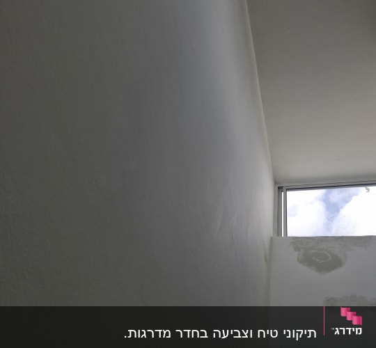 קיר לבן עם סימני תיקון צבע ליד חלון
